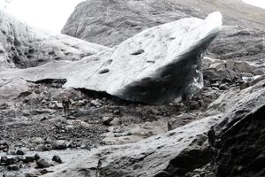 A man hiking across an iceburg, with a huge chunk of ice the size of two double decker busses next to him