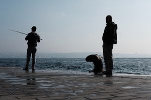 Two man stand on the tiled bank of a river, fishing